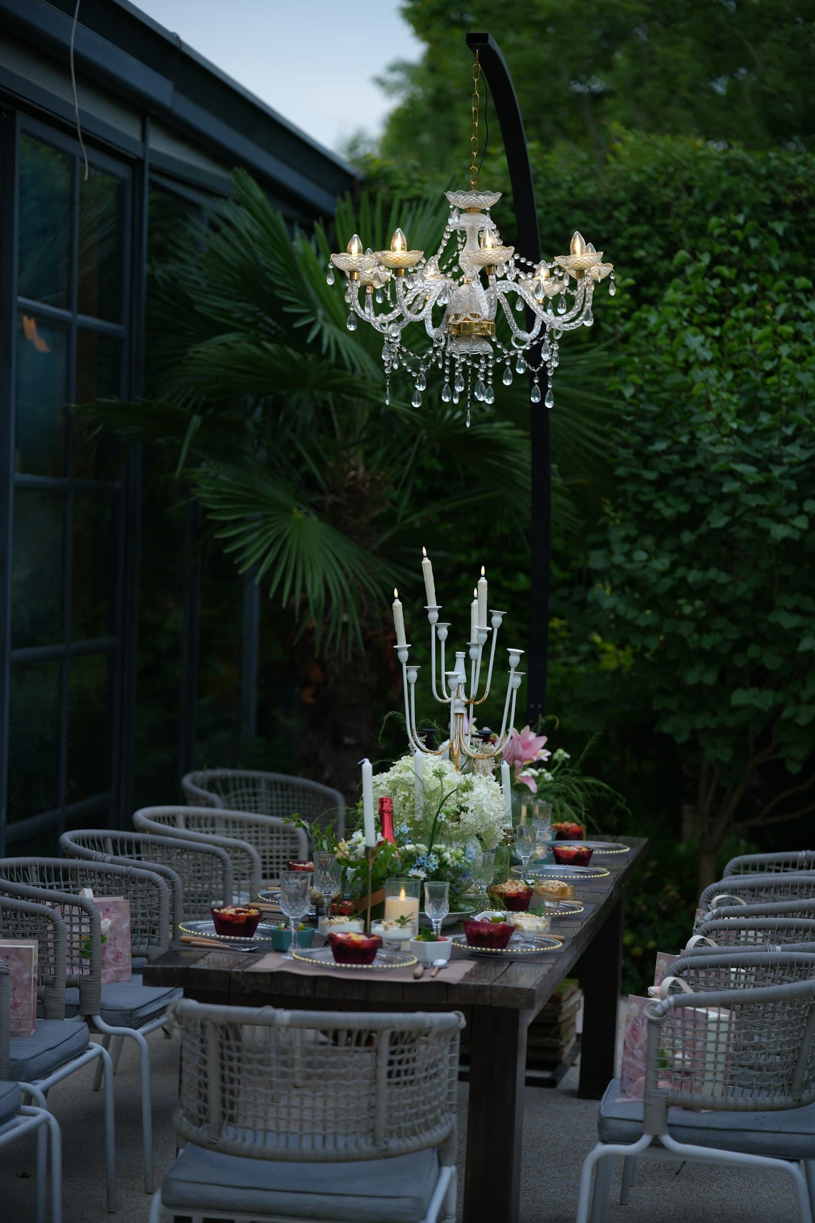 A crystal chandelier suspended over a candlelit garden dinner table